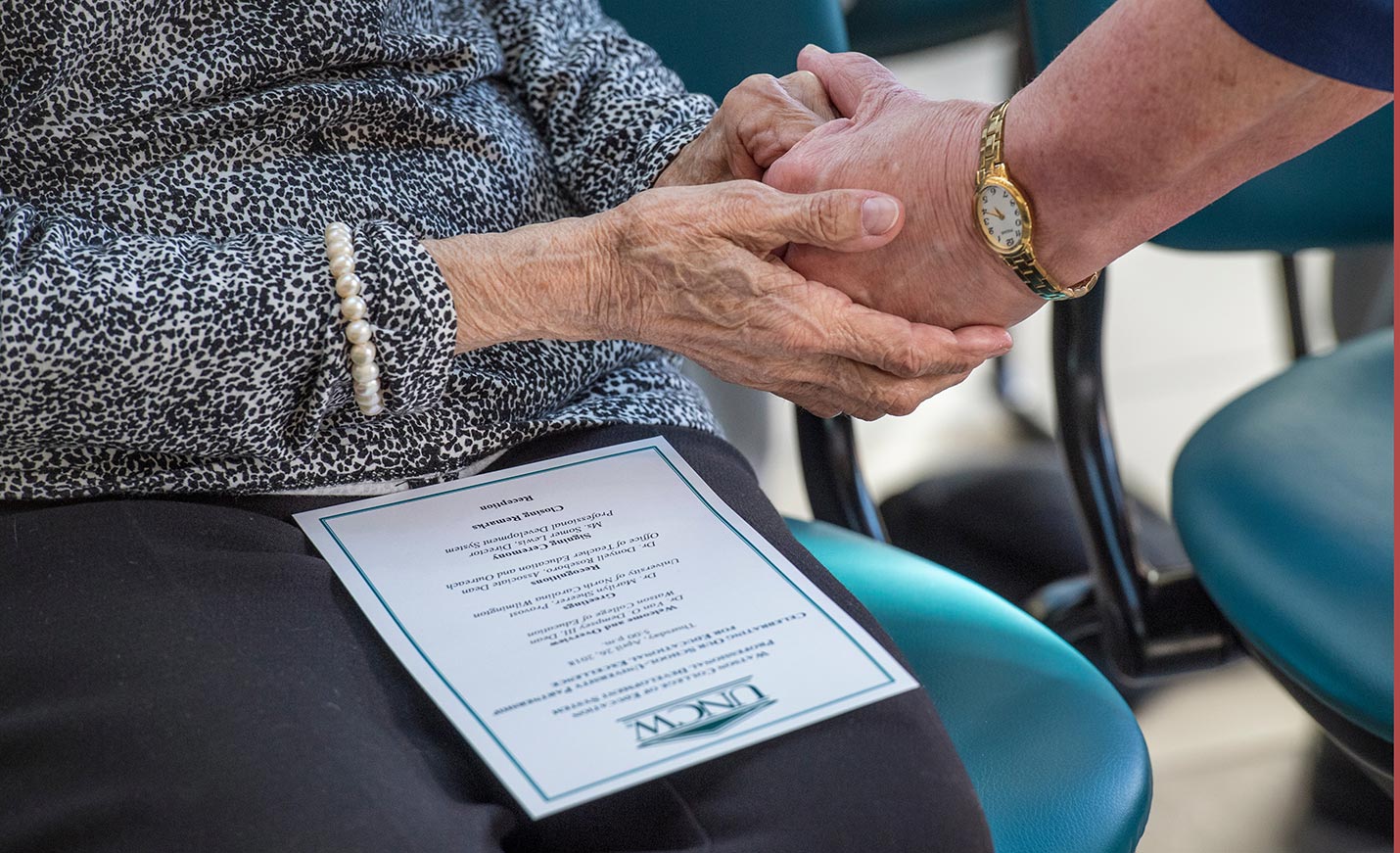 A close up of the hands of two older adults as they hold hands.