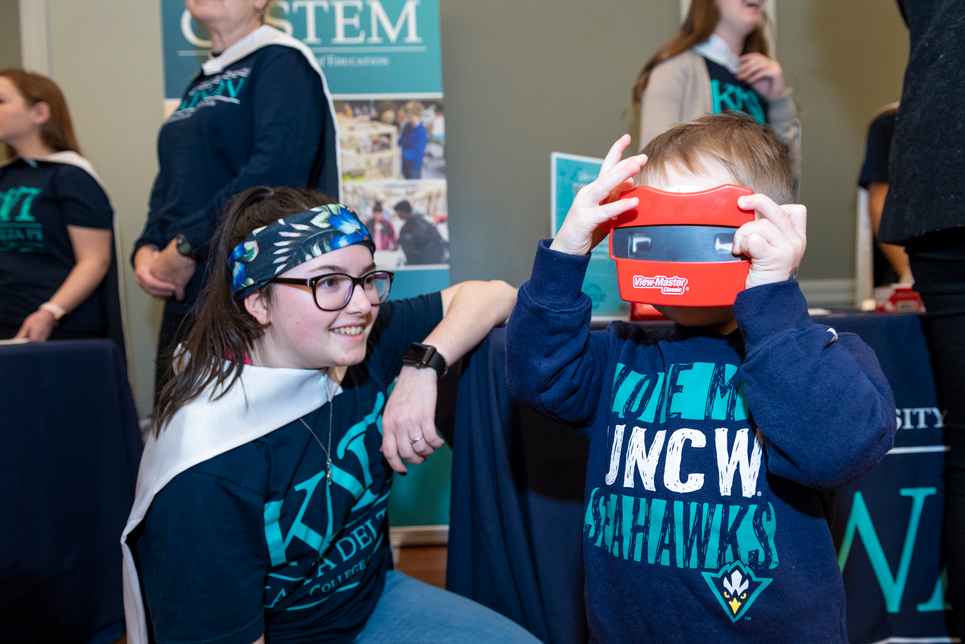 Elementary student lookinig through a viewmaster while a Watson student looks on