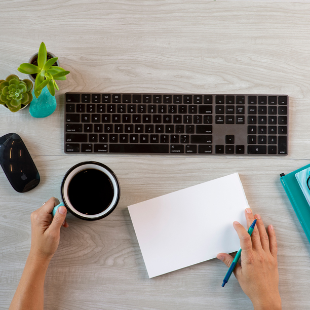 Ariel shot of a desk with a keyboard, mouse, notebook and cup of coffee.