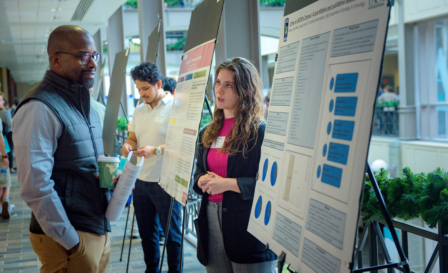 A student explains her research poster to a man during a student research showcase