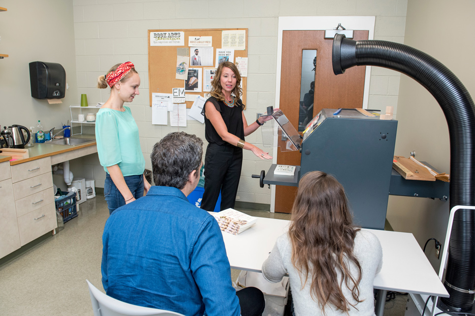 Teacher explains how the publishing lab equipment works to three students.