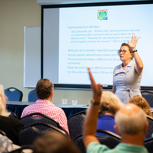 Teacher giving presentation holding up a hand asking for volunteers.