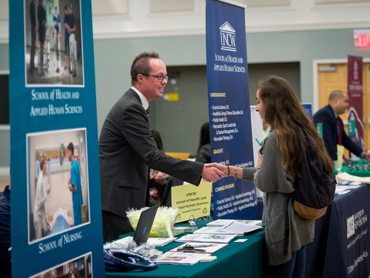 CHHS representative shakes hands with a student over a table