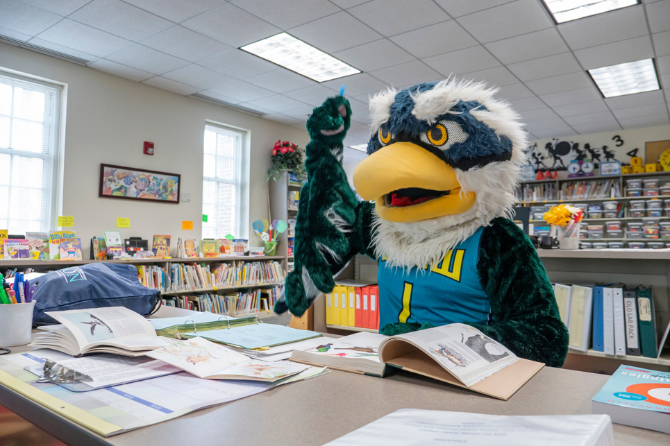 Sammy Seahawk reading a book in a classroom