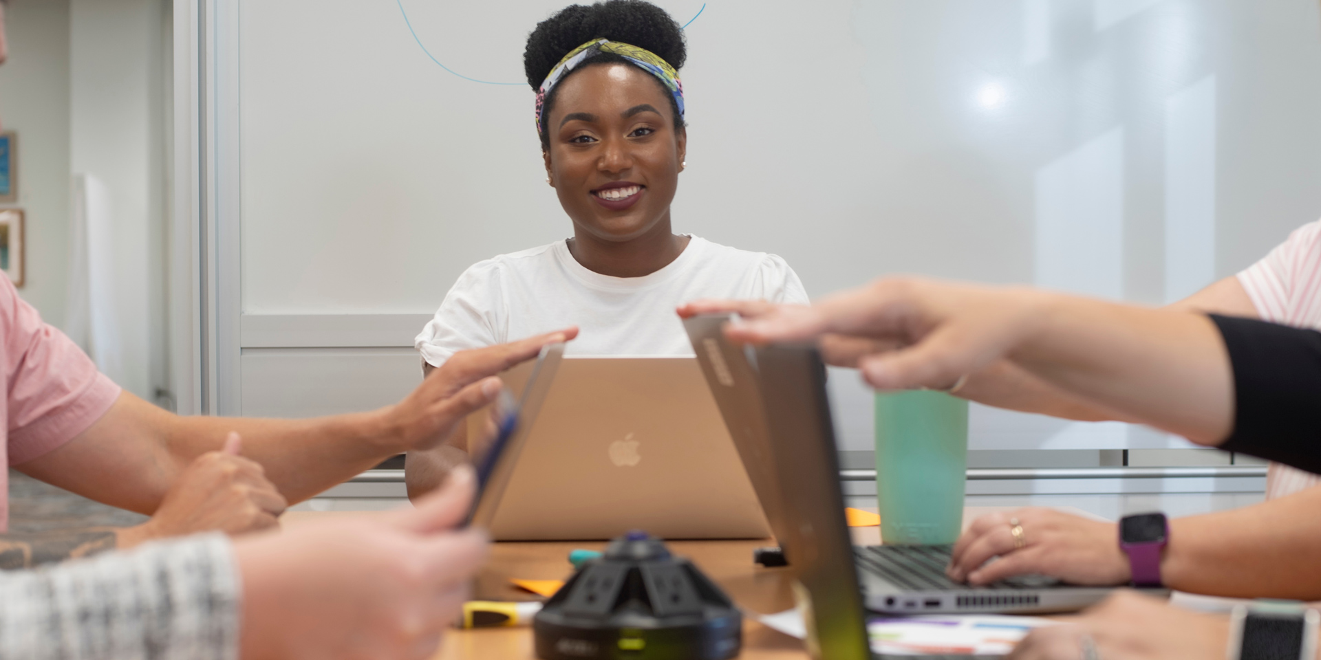 A person smiles at the camera during a meeting with people off camera