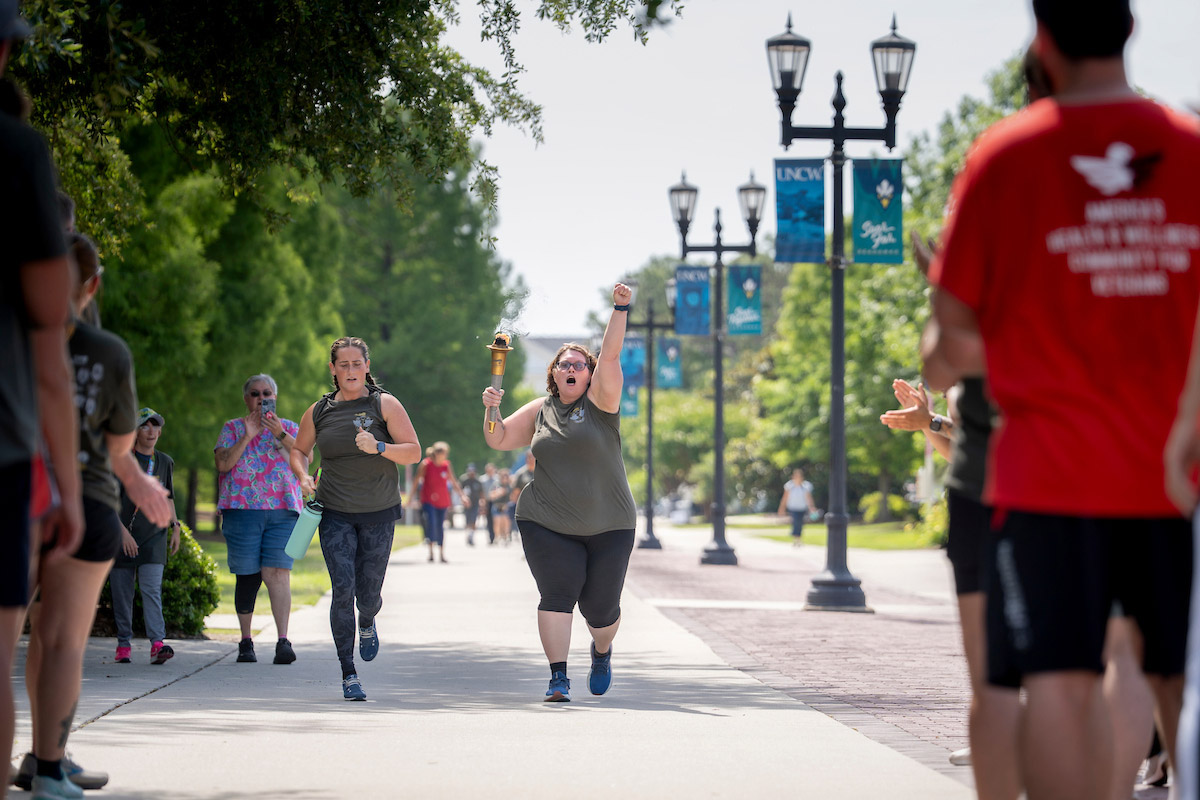 Runners on Chancellors Walk, one carrying a torch with her other fist in the air