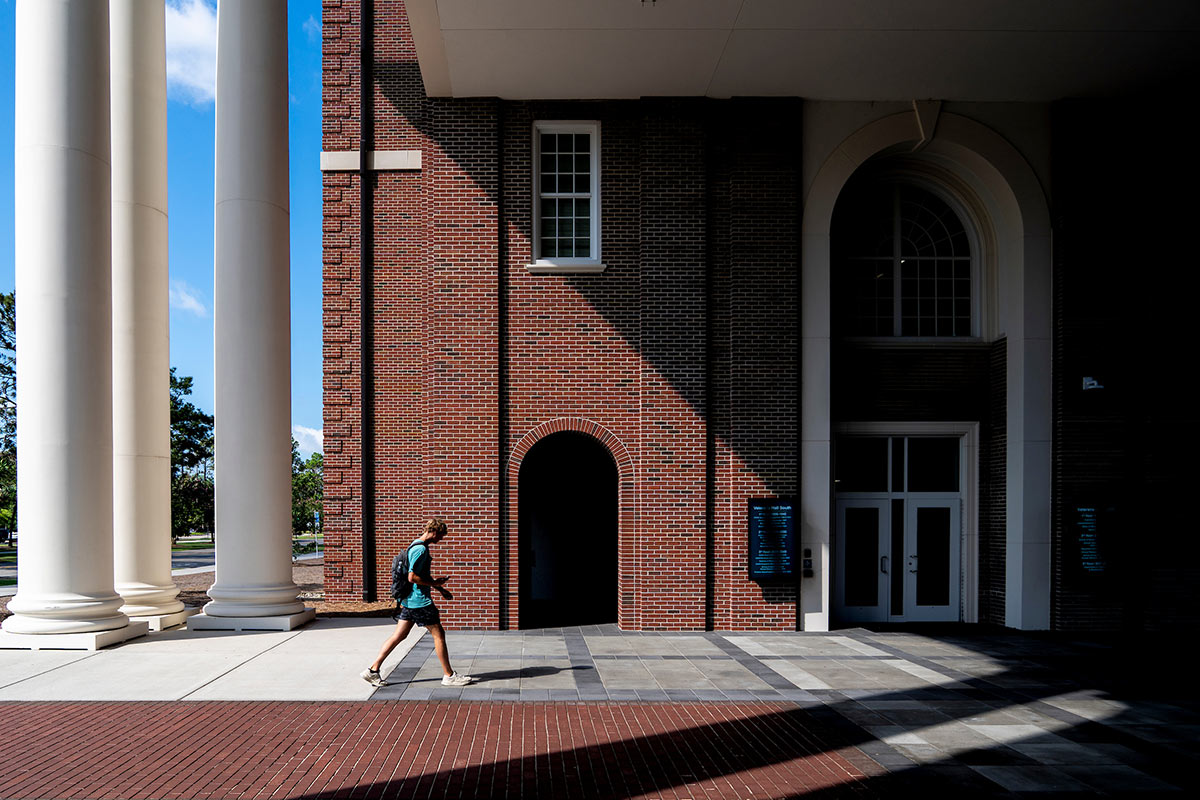 Mid-morning sun casts shadows as a student walks through the Veterans Hall breezeway