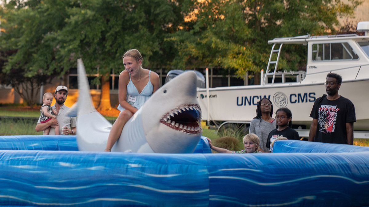 Alumni families watch as woman rides inflatable shark