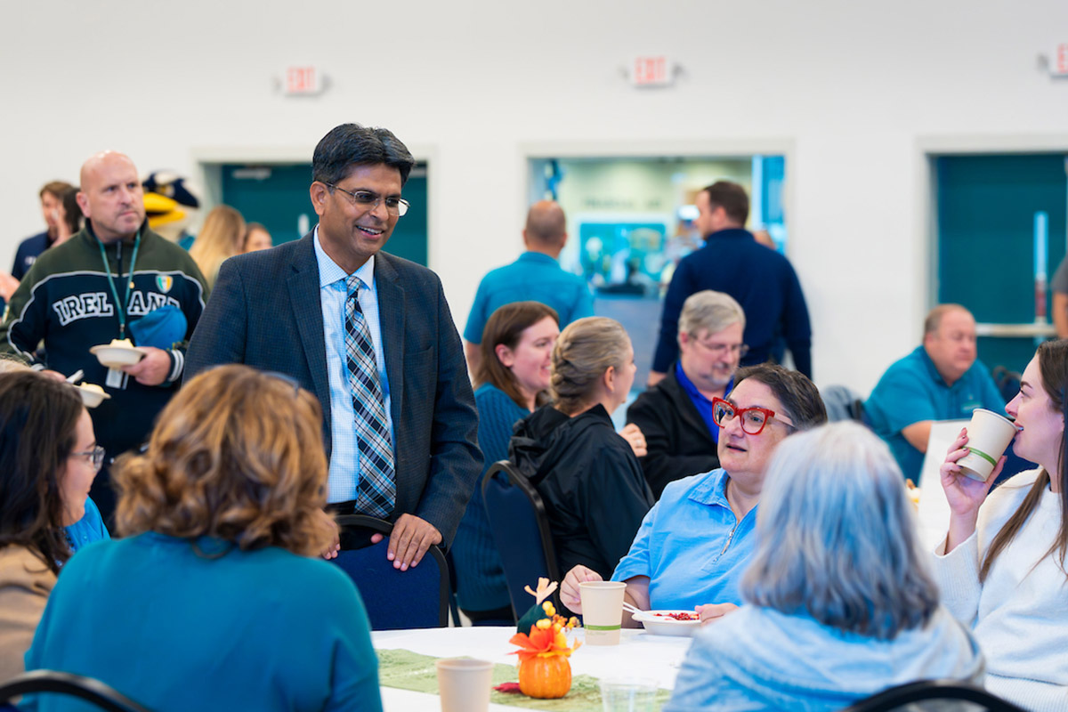 Chancellor Volety stands while talking to employees sitting at a table in the Warwick Center Ballroom