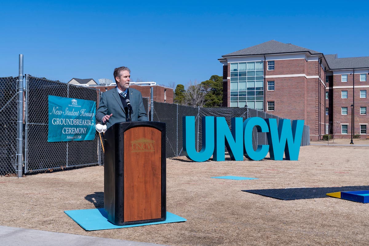 Kevin Meaney behind a lectern on the future site of new student housing