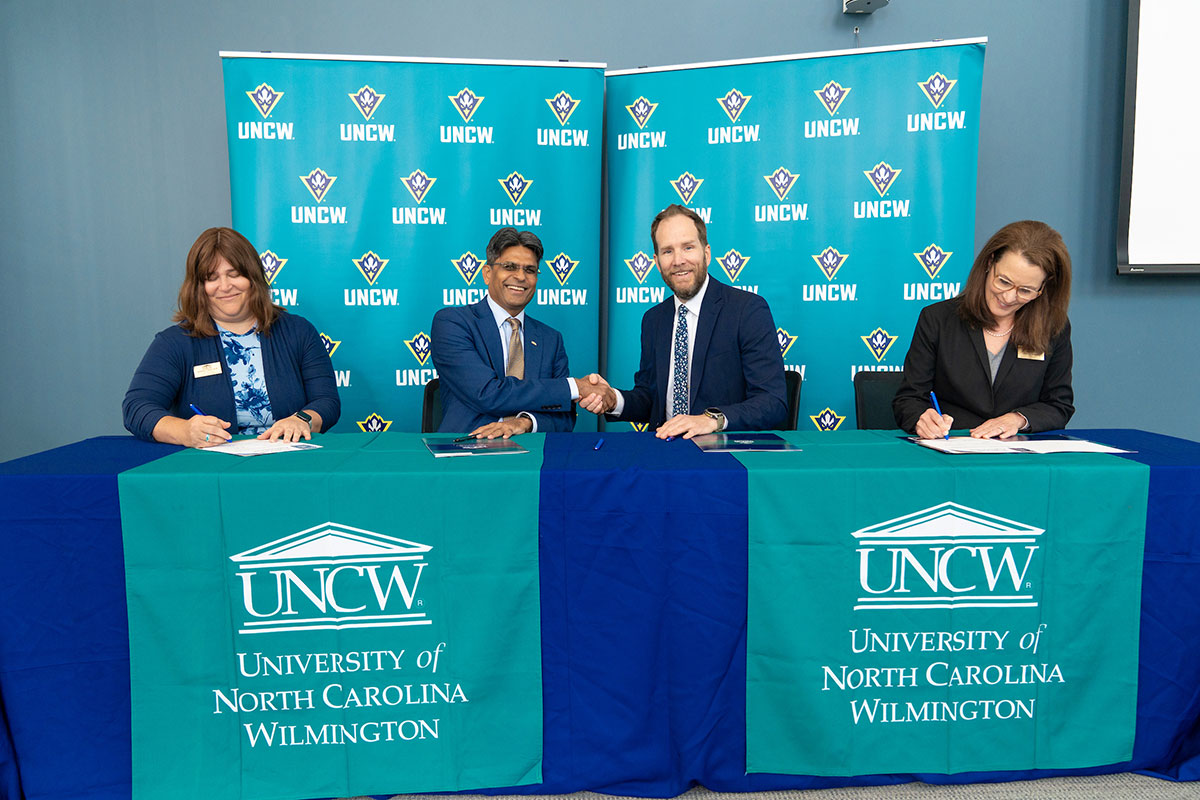 Chancellor Volety shakes hands with Andrew Kelly while Stephanie Caulder and Tracy Linderholm sign documents