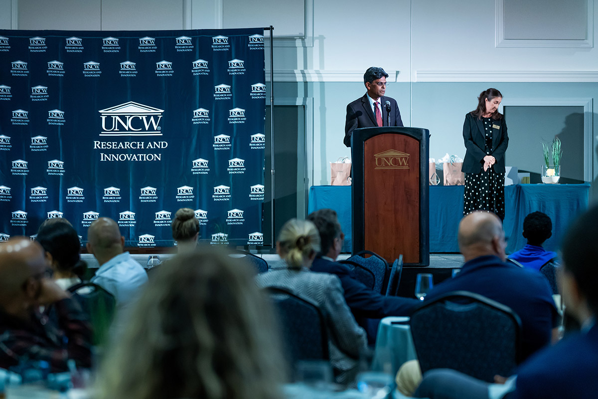 Chancellor Volety stands behind a lectern before a Research and Innovation backdrop
