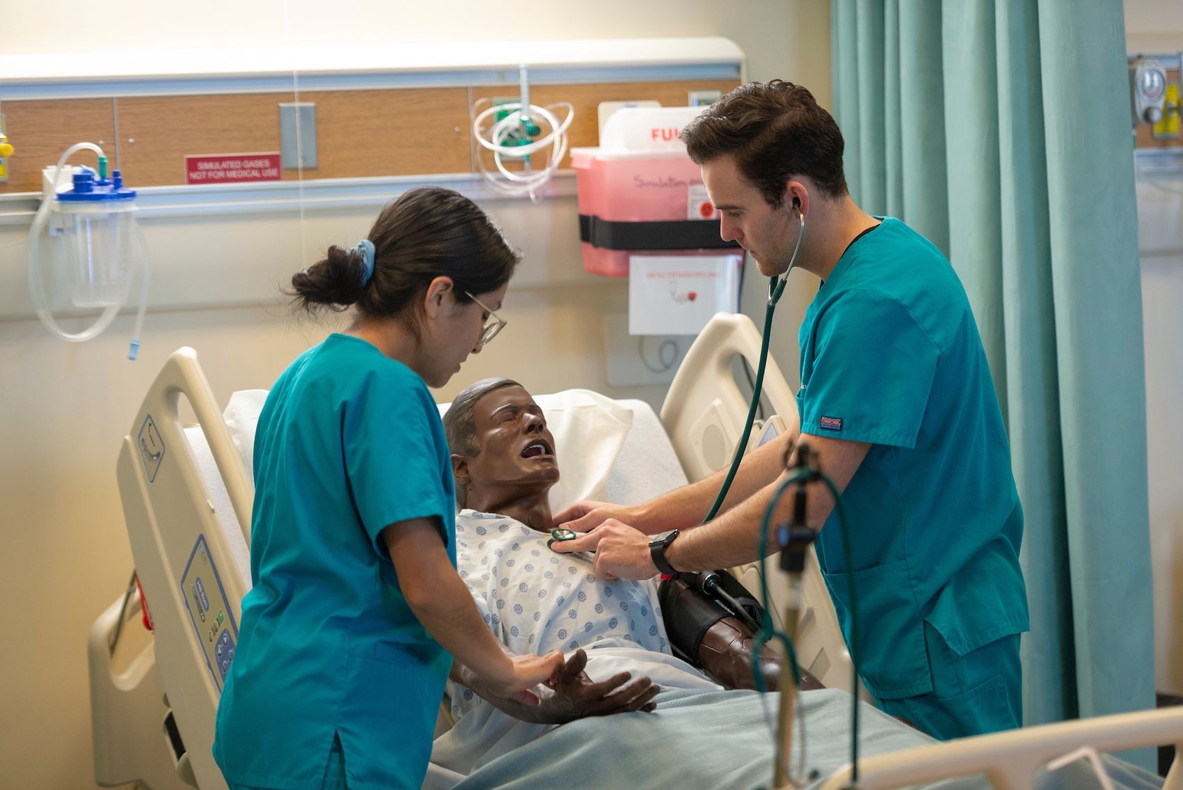 Two nursing students check the heartrate of a manikin during a simulation training.