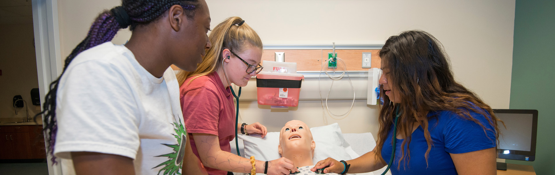 Three students do a medical examine on a practice mannequin.