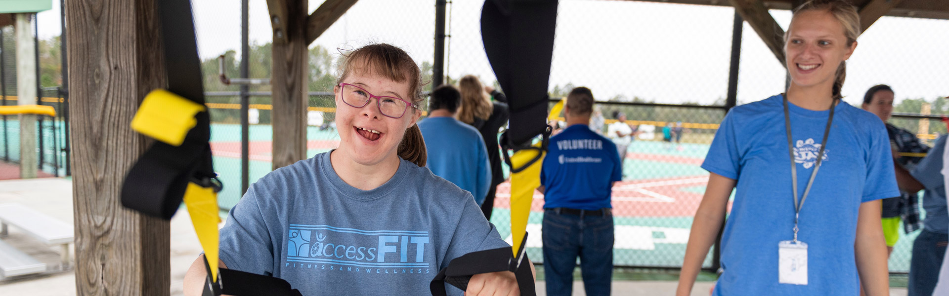 An accessFIT participant smiles while working out with the TRX cables while a recreation therapy student watches.