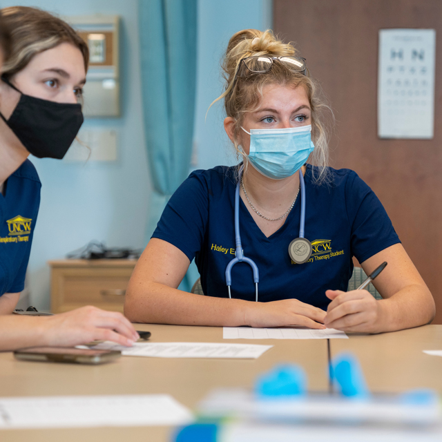 Nursing students sit at a table and take notes