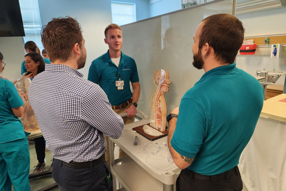 Three students gather around a model in the nursing simulation lab.