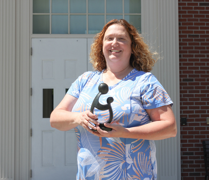 Dr. Tamatha Arms stands in front of McNeill Hall holding her DAISY award, a small statue - hand carved Healer’s Touch sculpture from Zimbabwe.