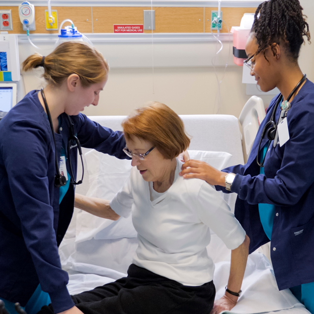 Two nurse students help a patient out of bed