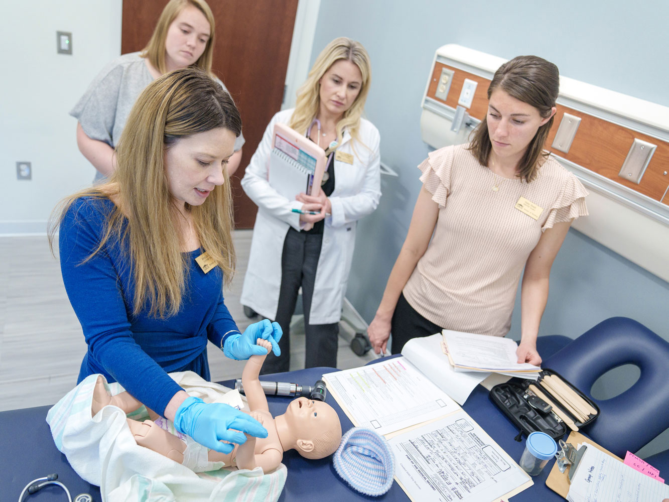 Three DNP students observe one other DNP student as she conducts an assessment on a manikin baby.