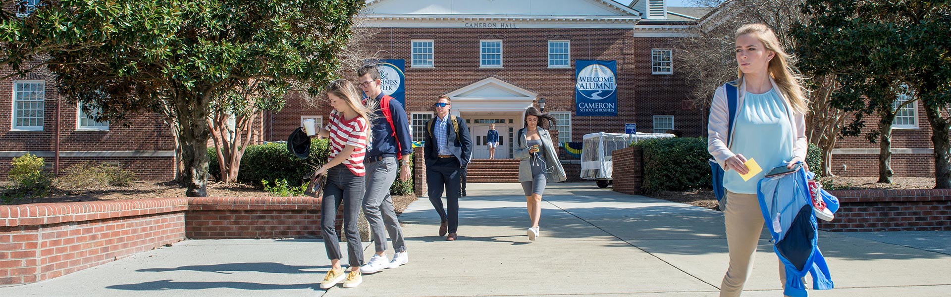 Outside view of Cameron Hall with students walking in and out and Business Week Banner Hung On Building