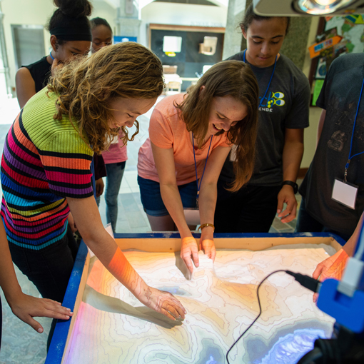 Students study a projection of a topographical map on a table