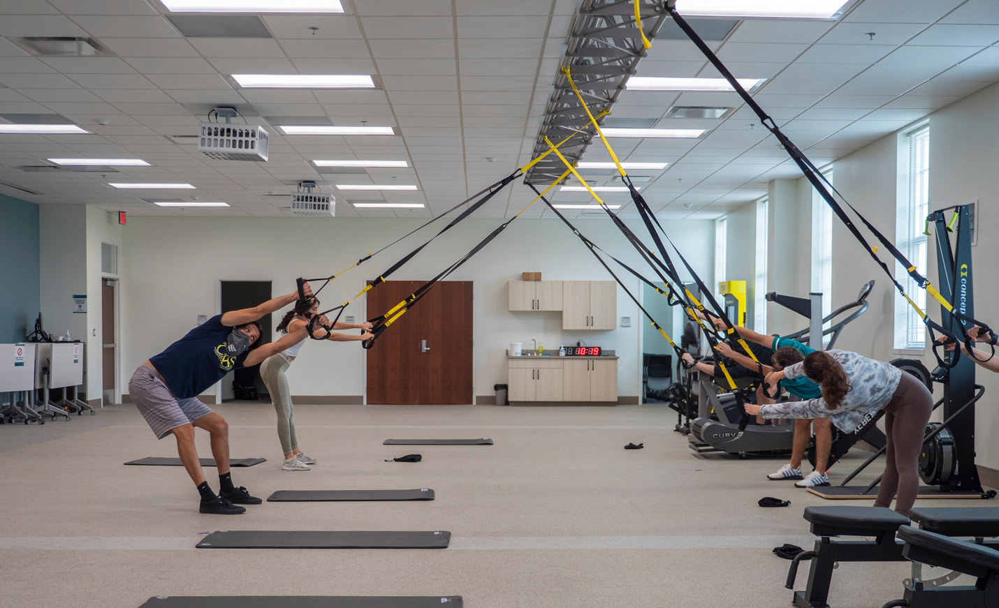 Students stretch using the TRX All-in-One Suspension Training System in a lab.