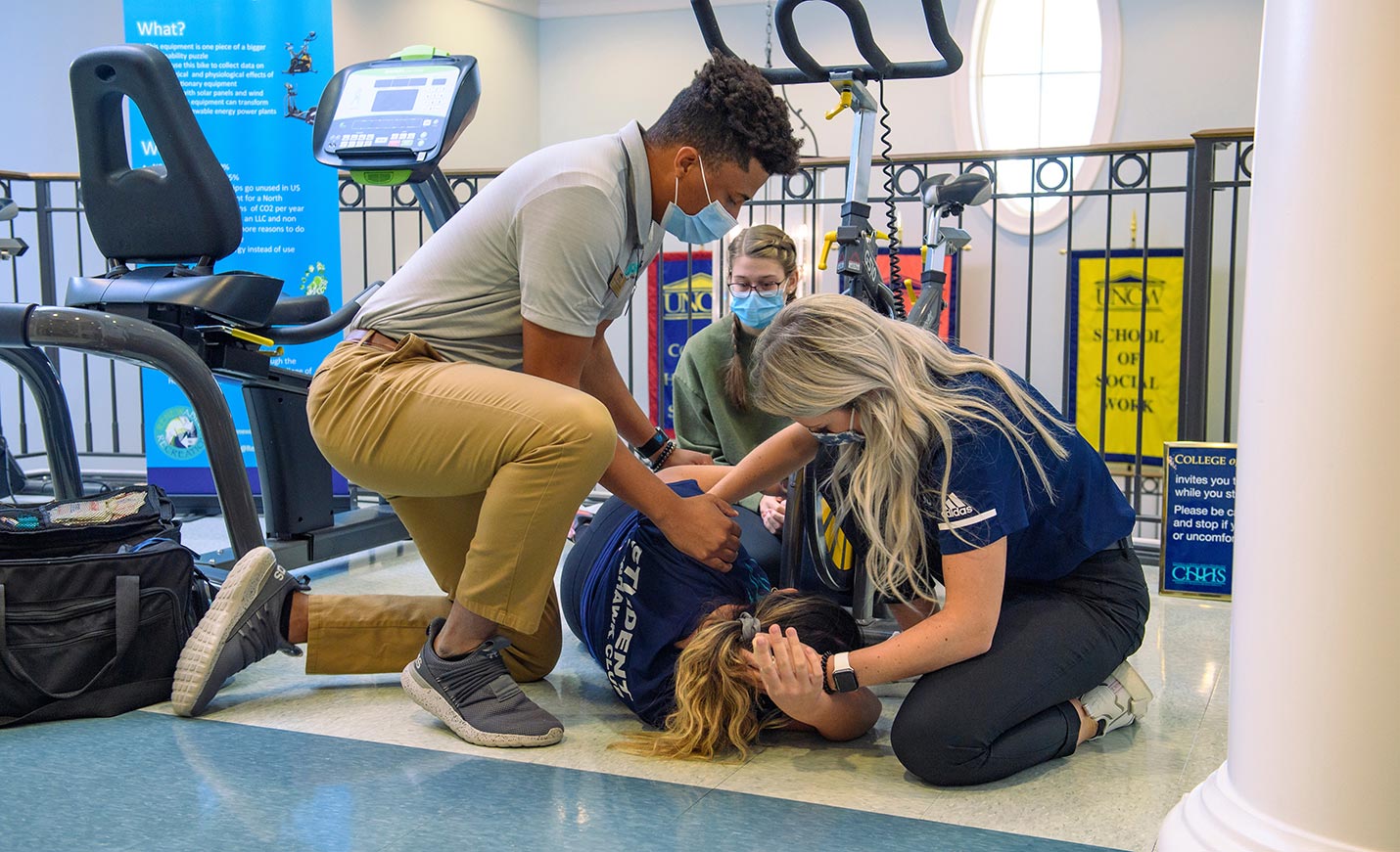 Two athletic training students practice treating an injured patient on the floor.