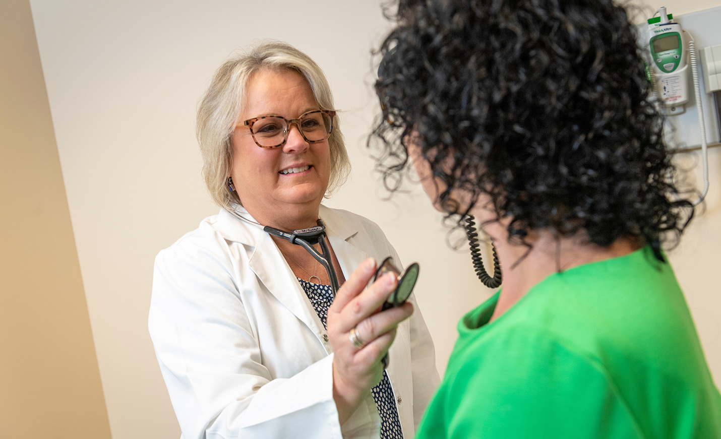 A nurse holds a stethoscope near the chest of a patient.