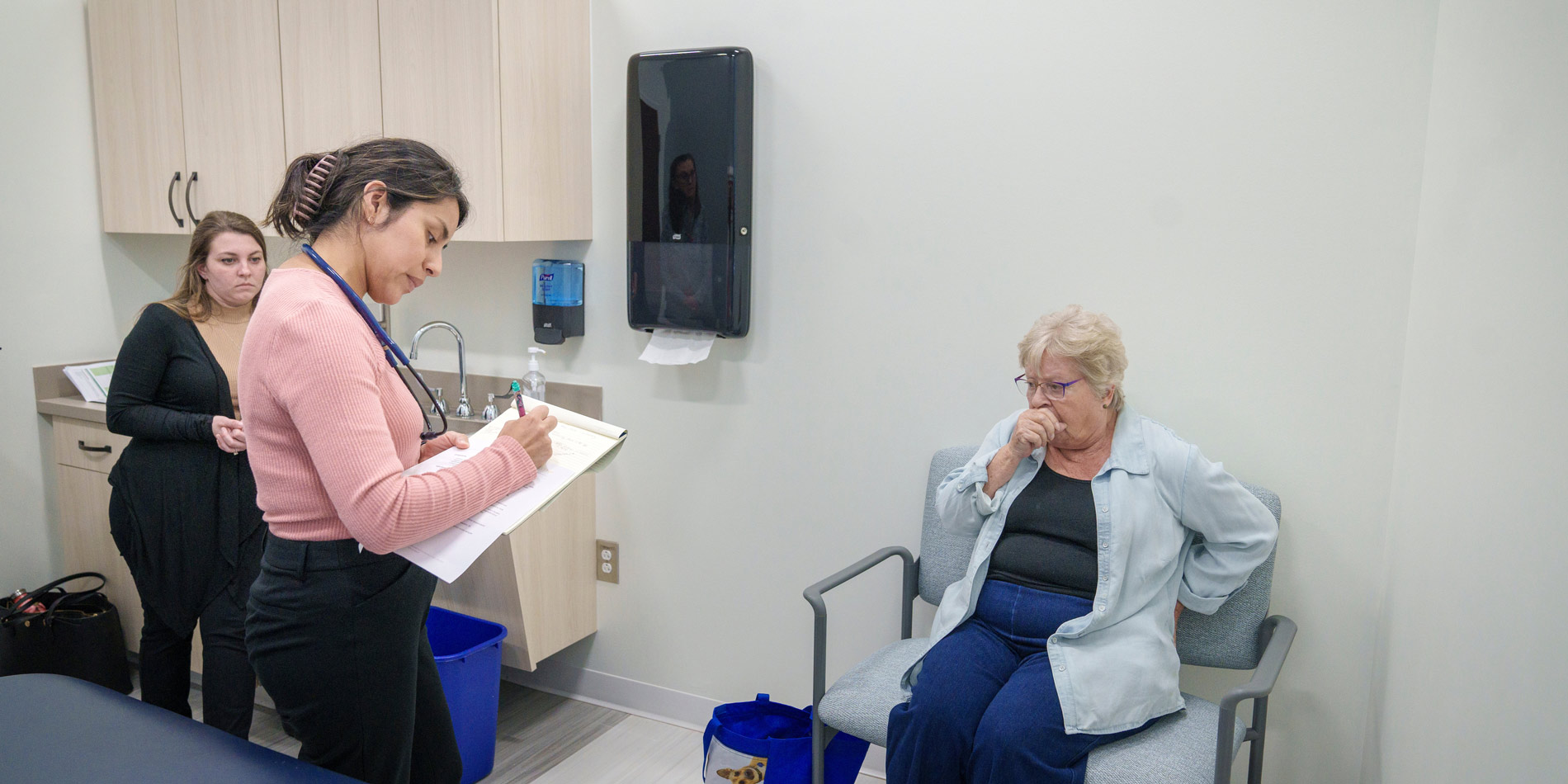 A nursing student writes on a clipboard while practicing an examination of an older adult patient..