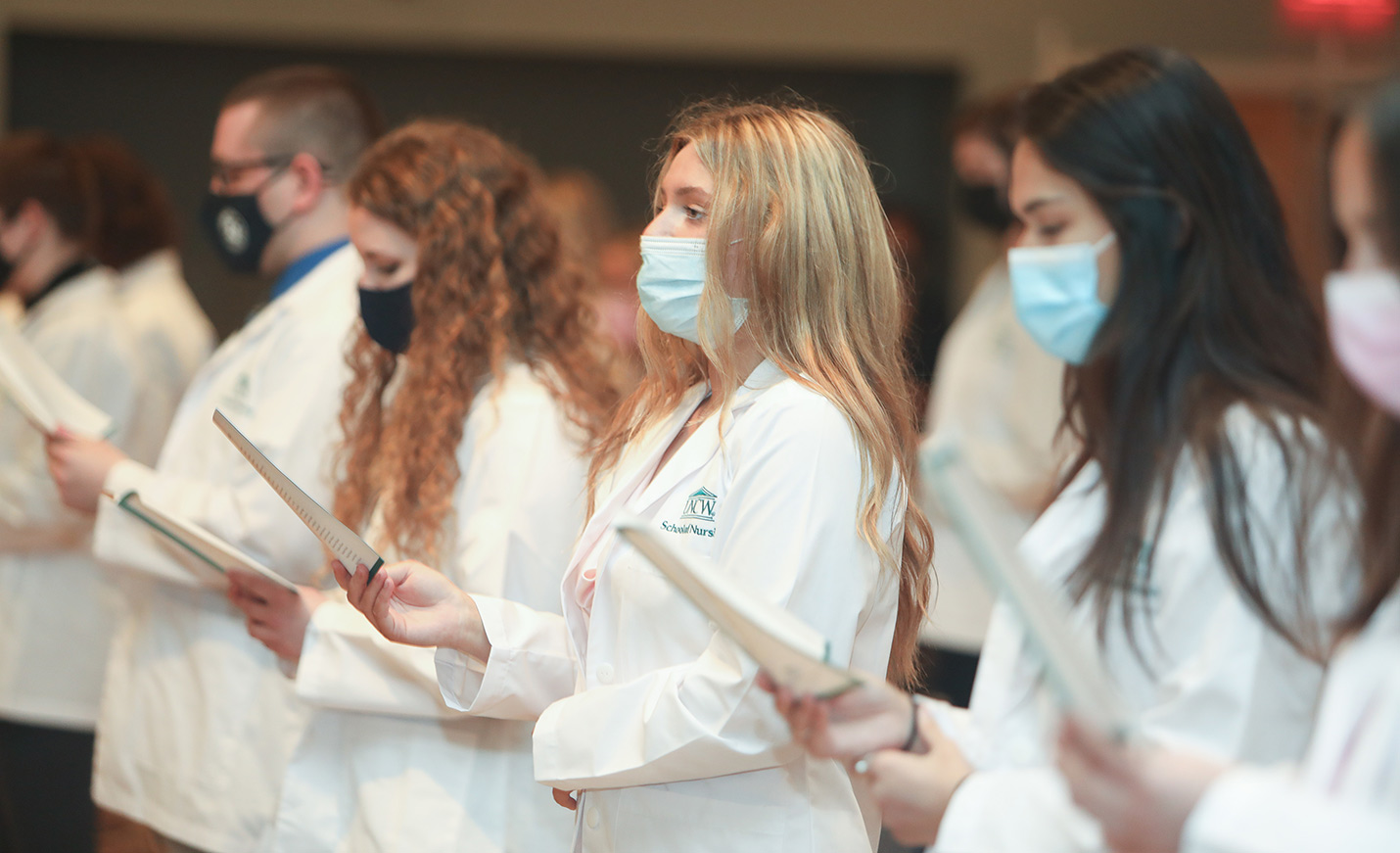 nursing students in white coats standing for their White Coat Ceremony. 