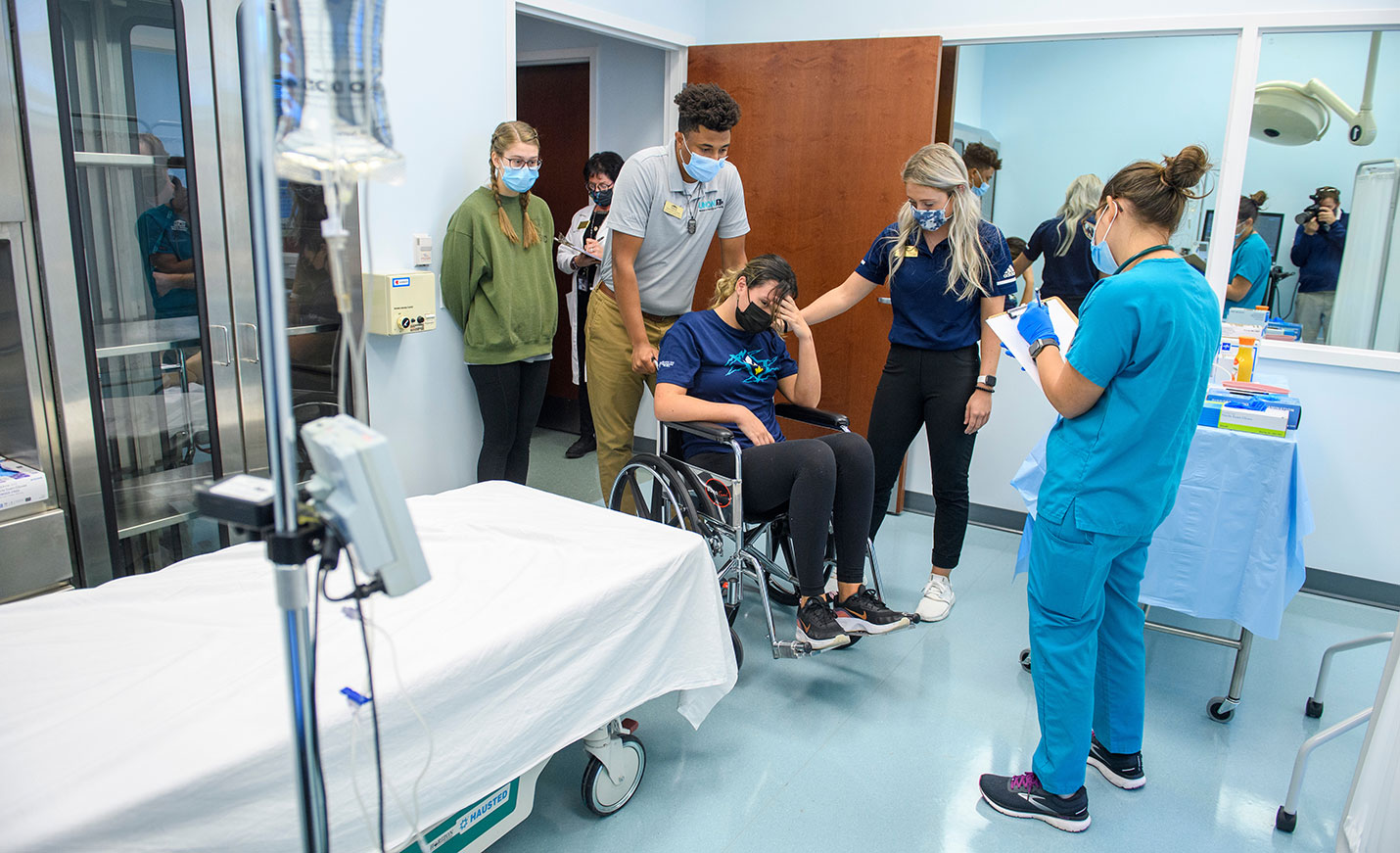 A nursing student and athletic training students work together to treat a patient in a wheelchair in a classroom simulation.
