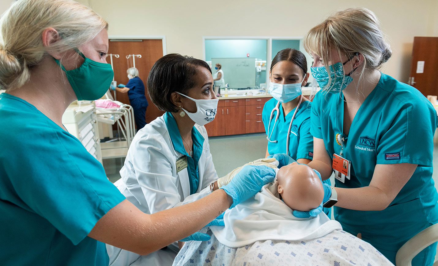Three nursing students practice delivering a baby mannequin while their nursing instructor assists. 