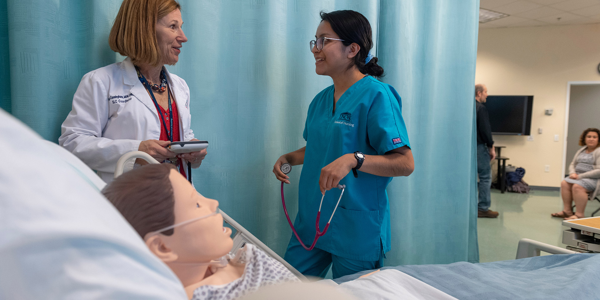 A nursing student and a doctor talk beside a manakin dressed as a patient