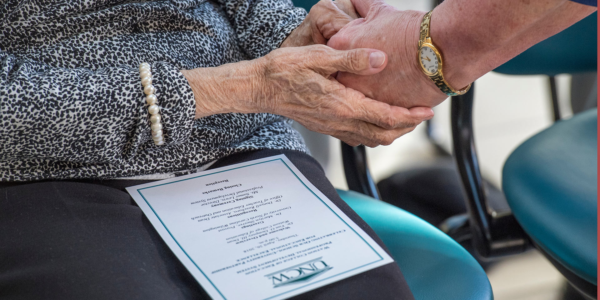 Two people off screen holding hands next to a program for a UNCW event