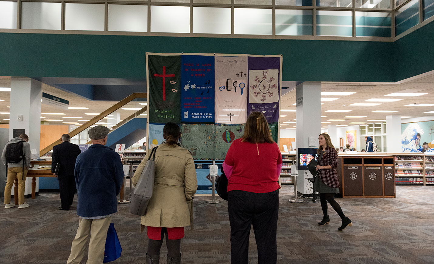 Three people stand with their backs to the camera as they look up at the AIDS quilt in Randall Library.