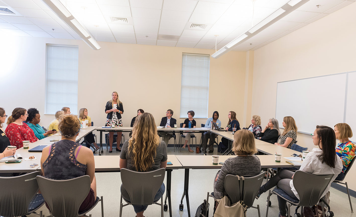 A group of faculty, staff, and students sit together around a square table discussing the #metoo movement.