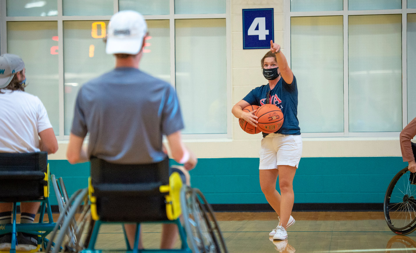 Students playing a game of wheelchair basketball while their instructor gives direction.