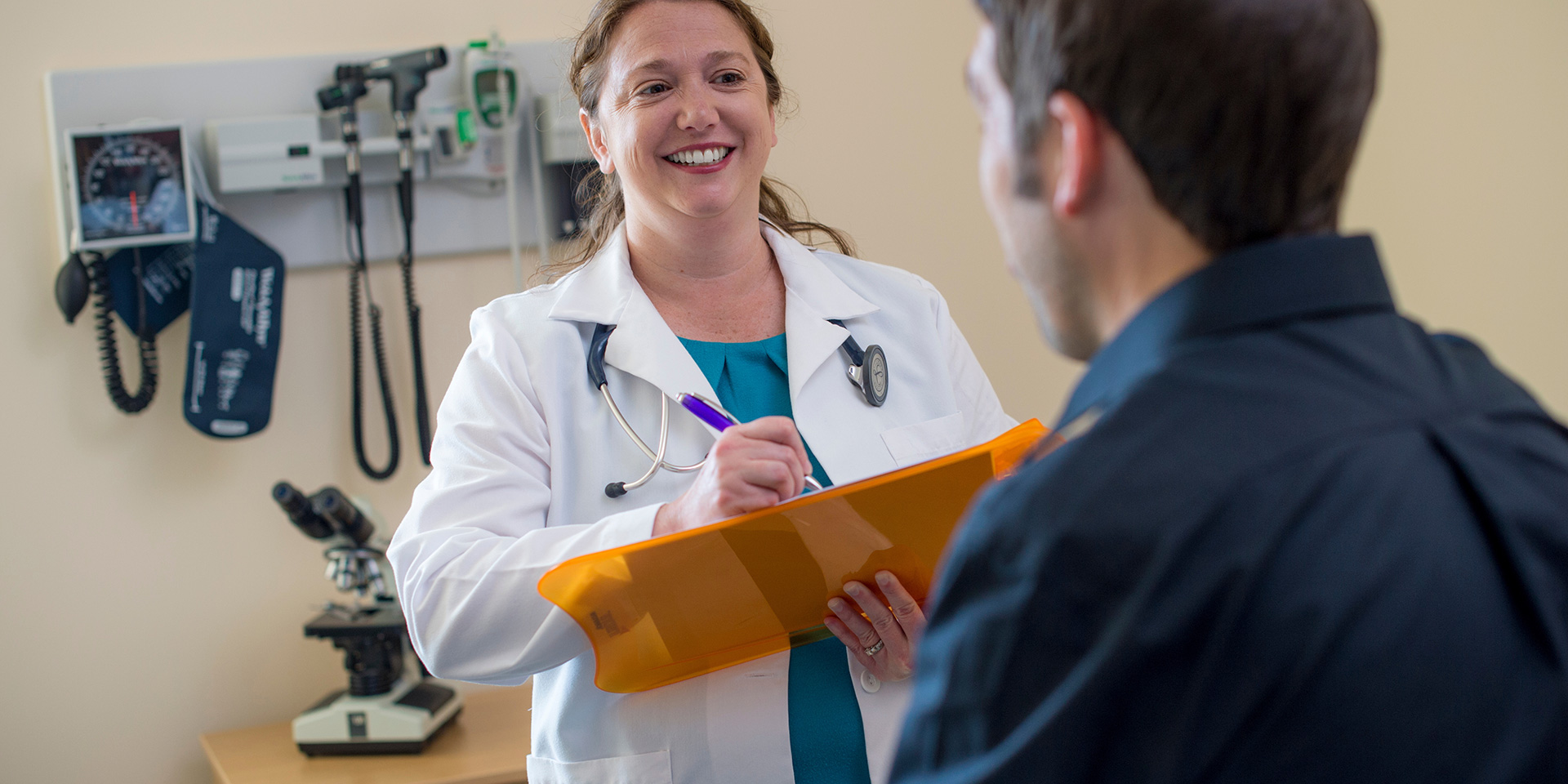 A doctor smiles at a patient while writing on a clipboard
