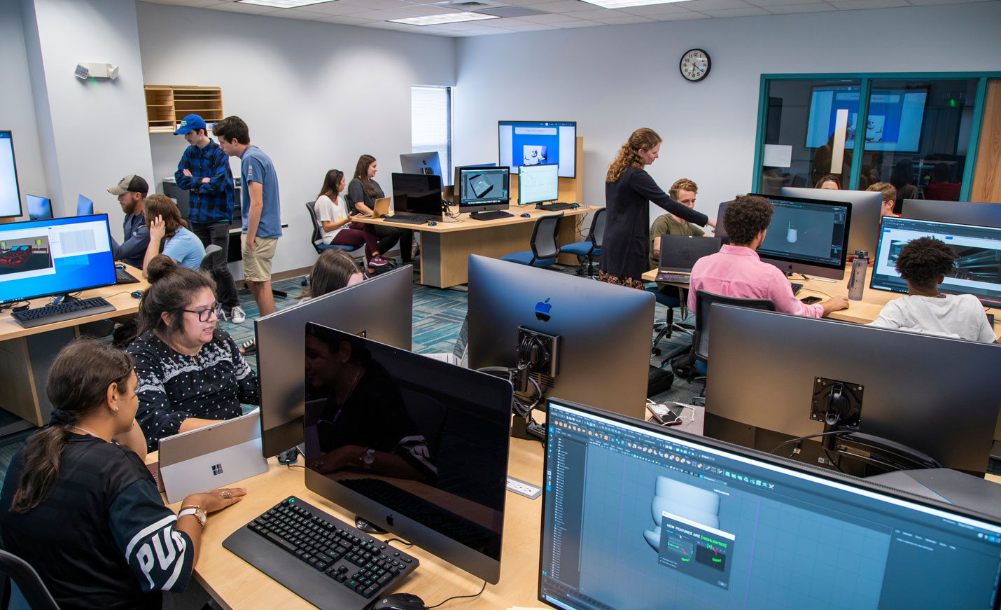 A class of students in a digital arts lab; an instructor is assisting one student