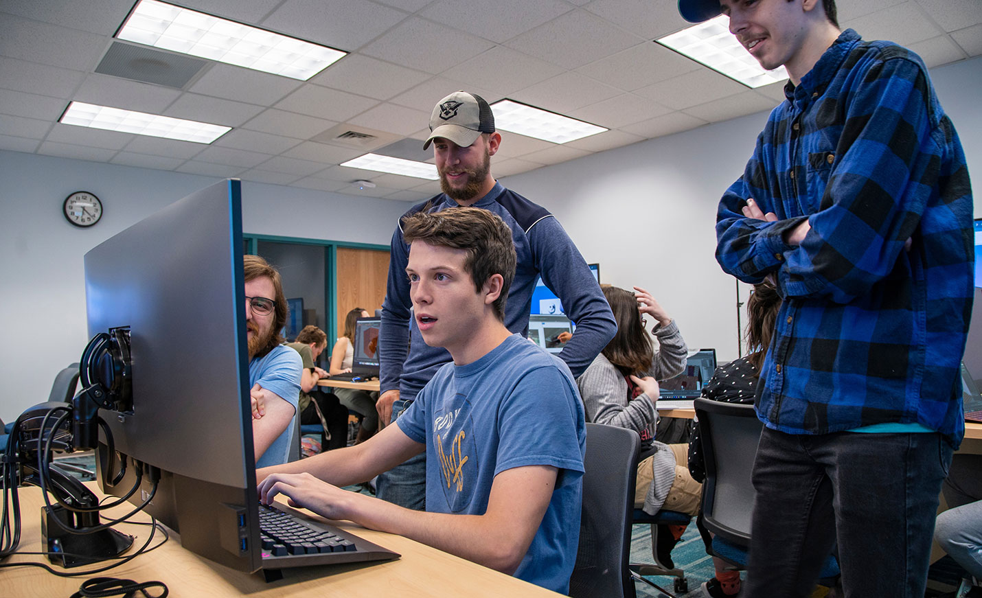 A student sits at a computer while two students standing behind him look on