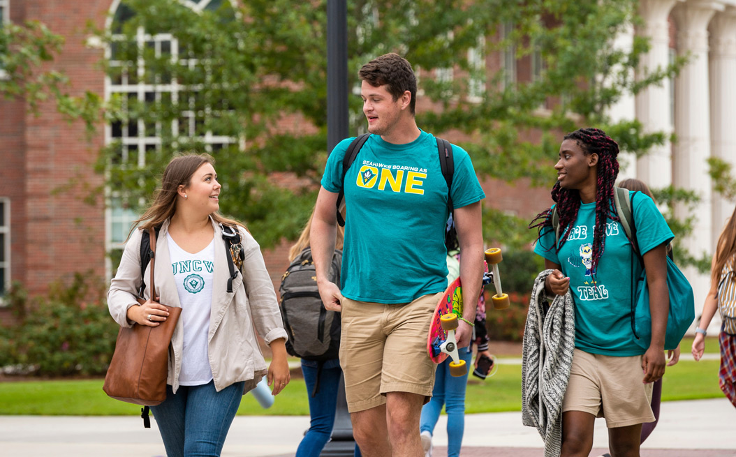 Three students wearing UNCW attire walking and talking on Chancellor's Walk