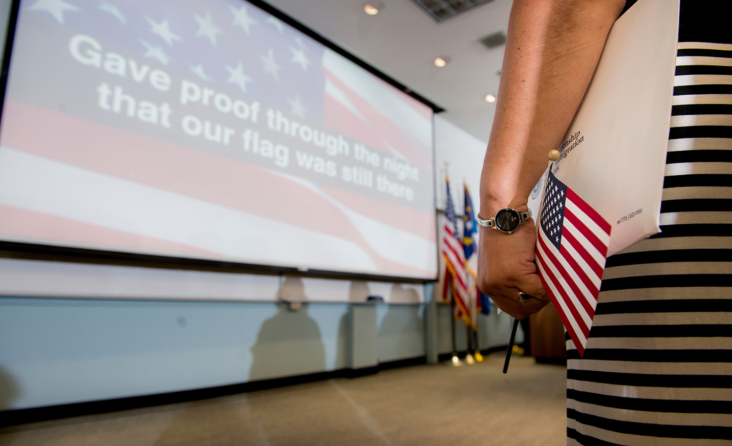 Words to the Star-Spangled Banner projected on a screen with an American flag in the background