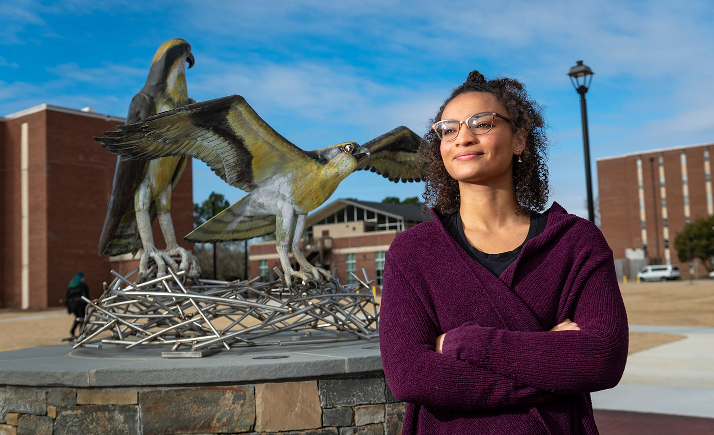 A student stands in front of a Seahawk nest statue