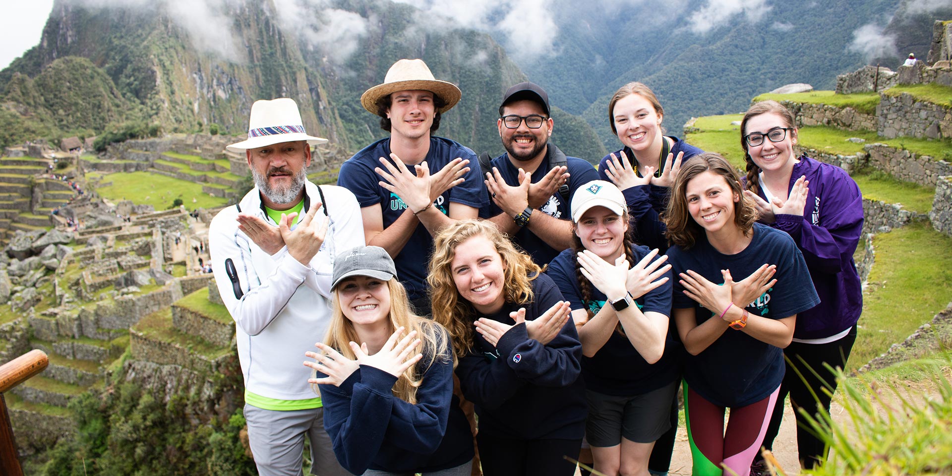 Students do the Wings Up hands in front of the Machu Picchu ruins