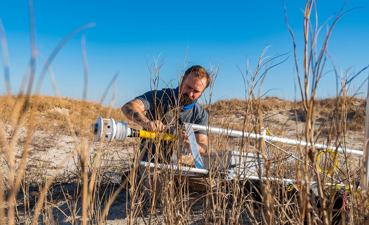 faculty member adjusting a weather measurement tool at the beach