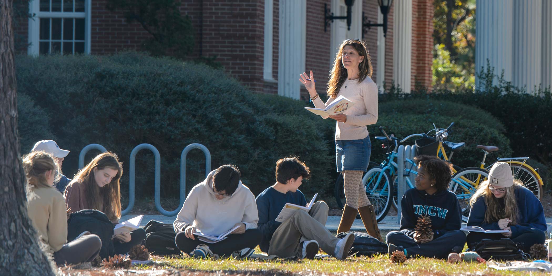 A professor reads from a book during a class outside
