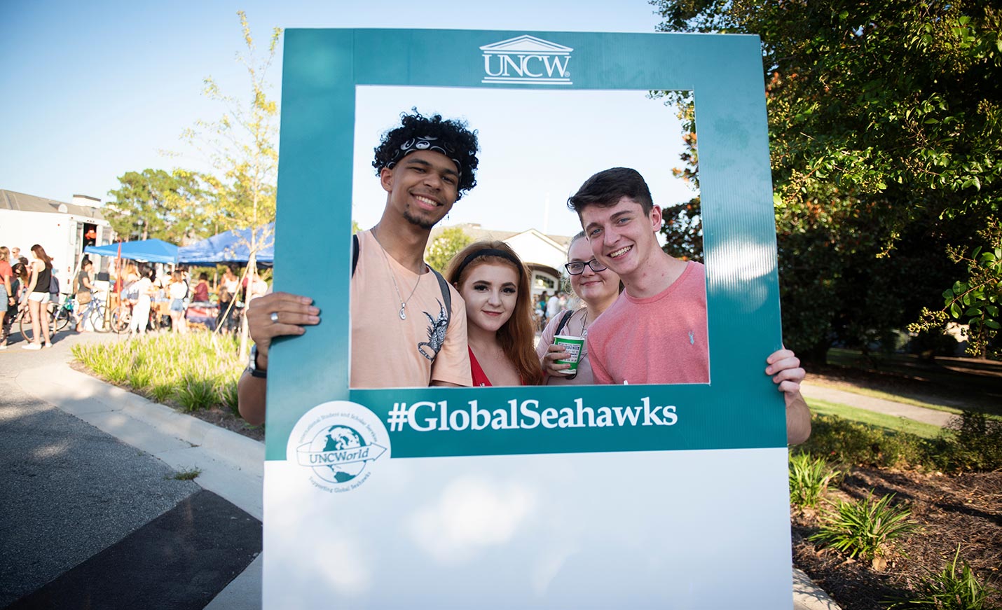 four students standing in a #globalseahawks picture frame
