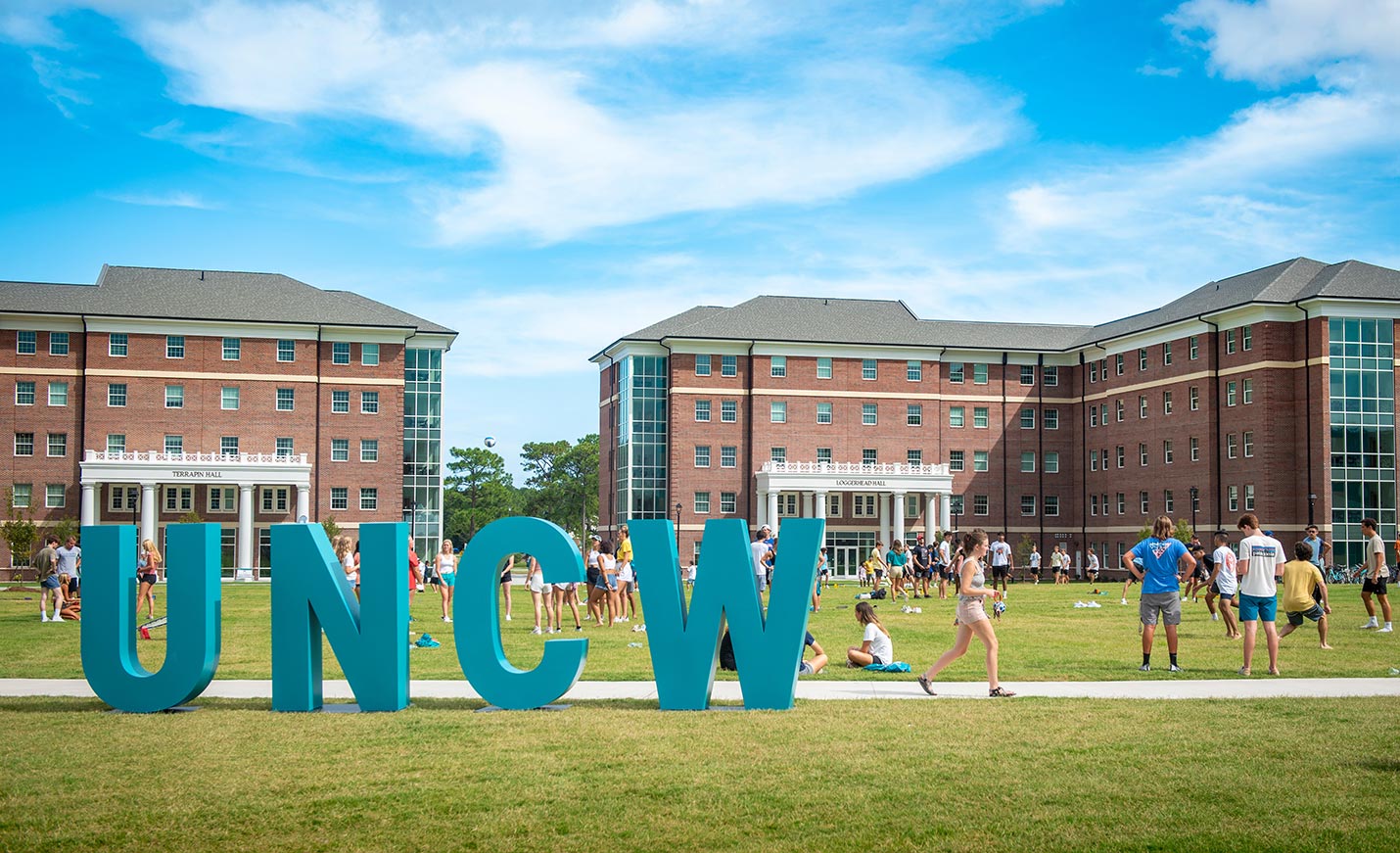 students relax by large UNCW letters near on-campus residence halls.