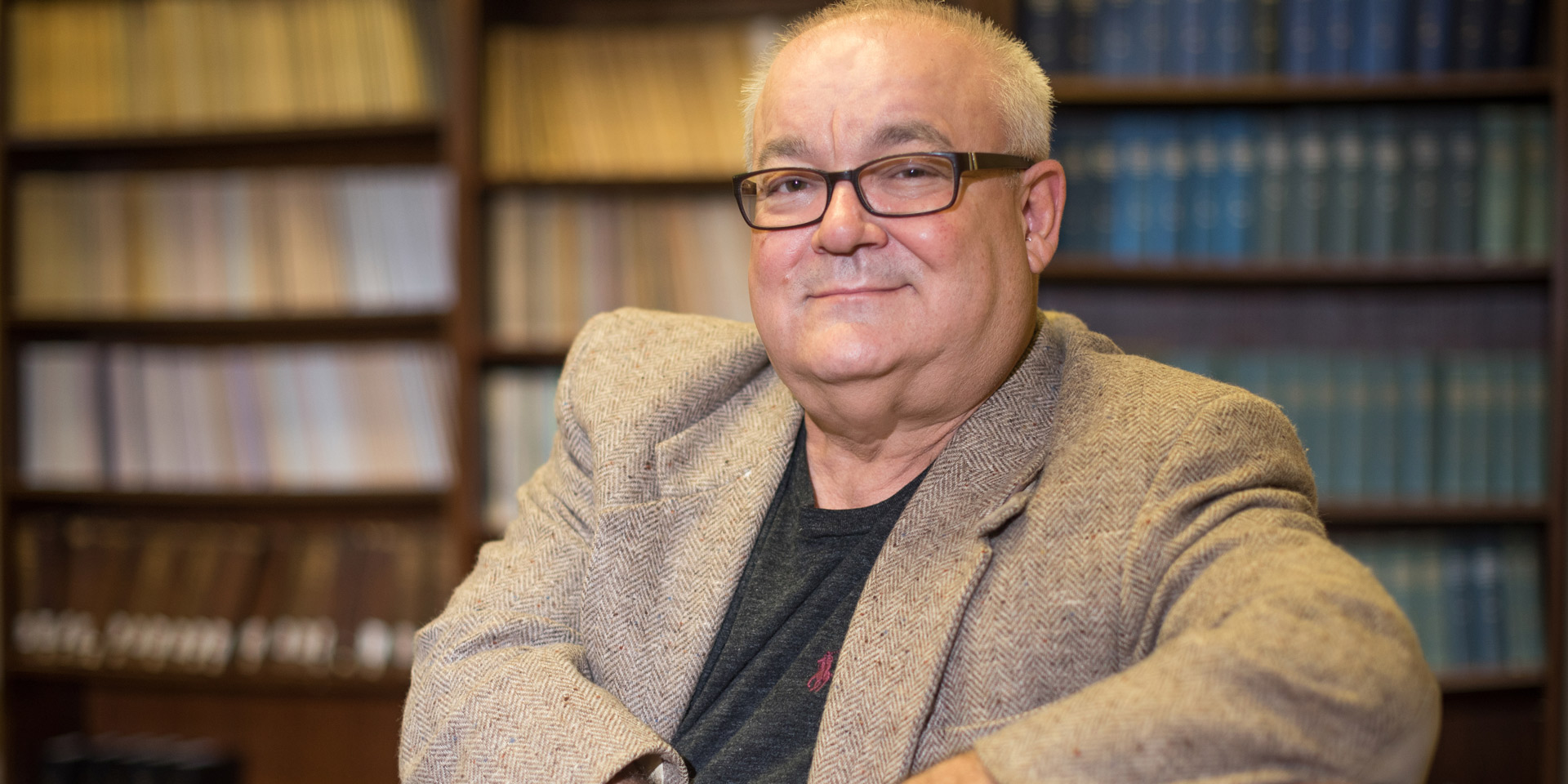 A history professor smiles for the camera in his office full of books